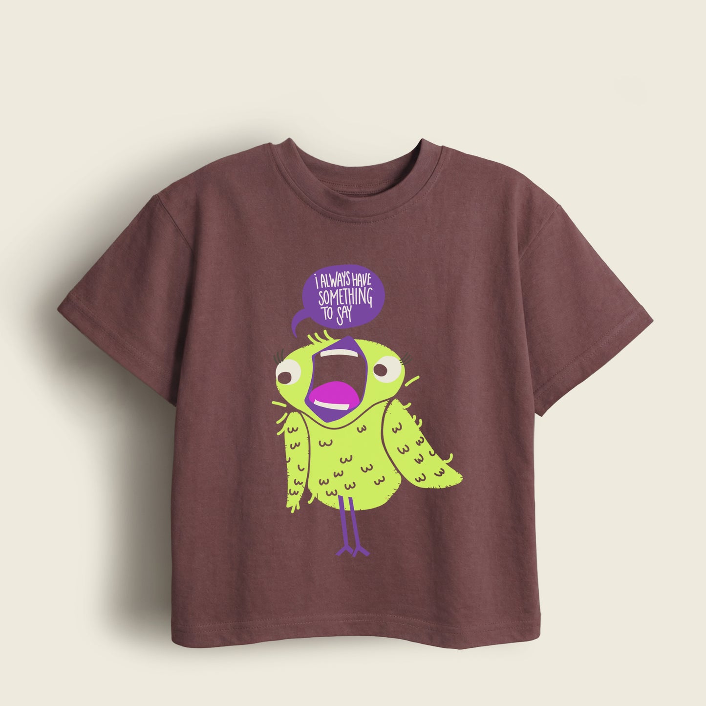Brown kids t-shirt with a lime yellow bird and purple speech bubble of 'I Always Have Something To Say' text on a beige background