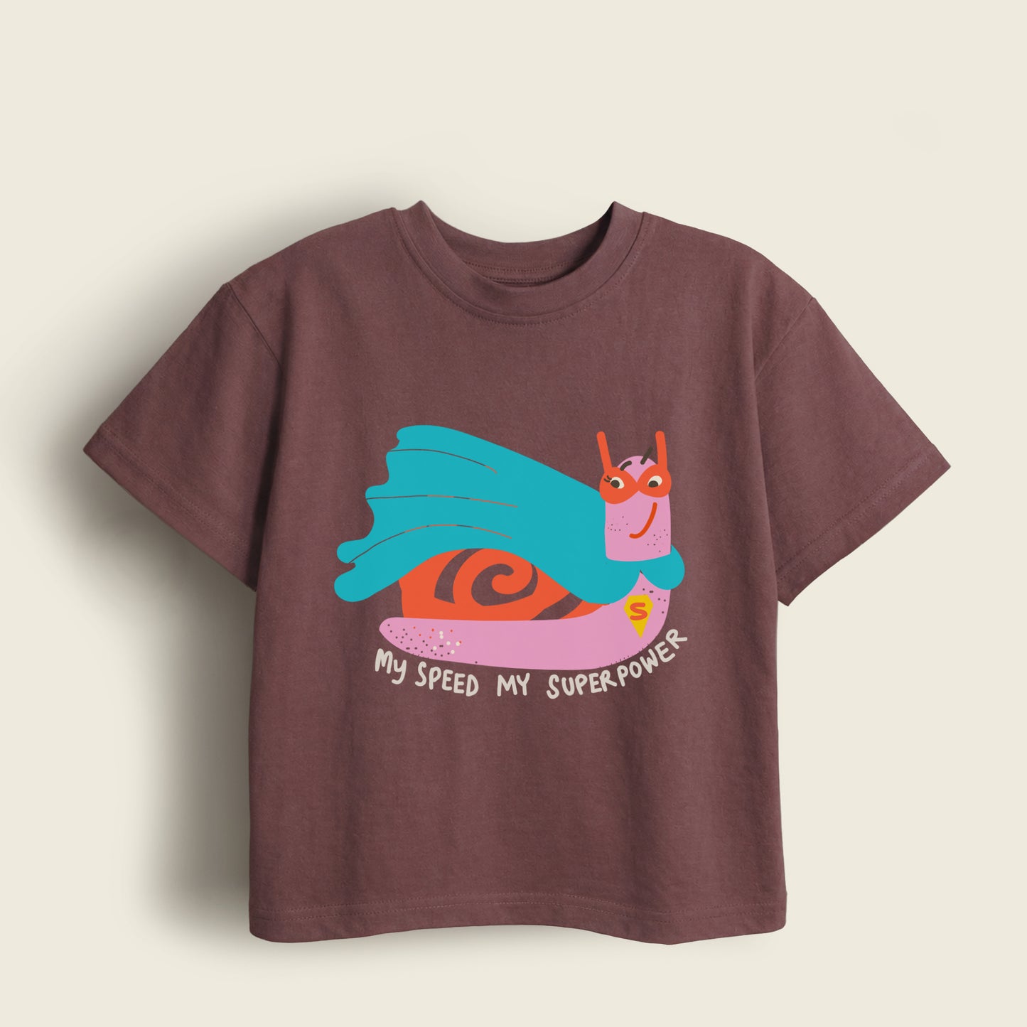 Brown kids t-shirt with a cape wearing snail graphic and 'My speed my superpower' text on a beige background