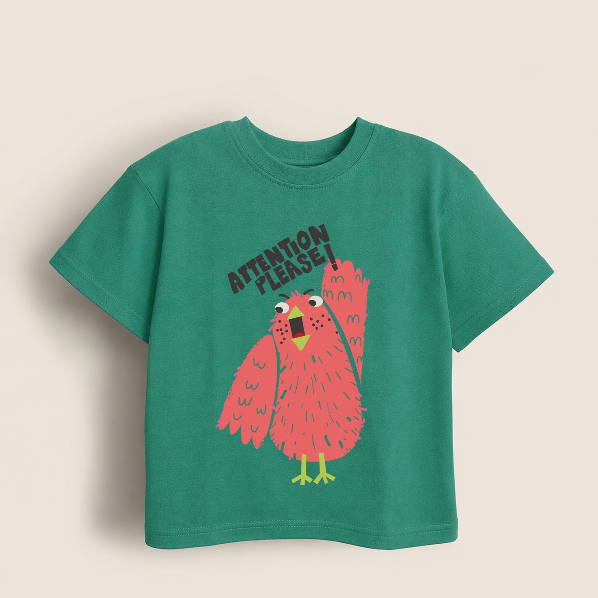 Green kids t-shirt with pink bird and 'Attention Please' text on a beige background