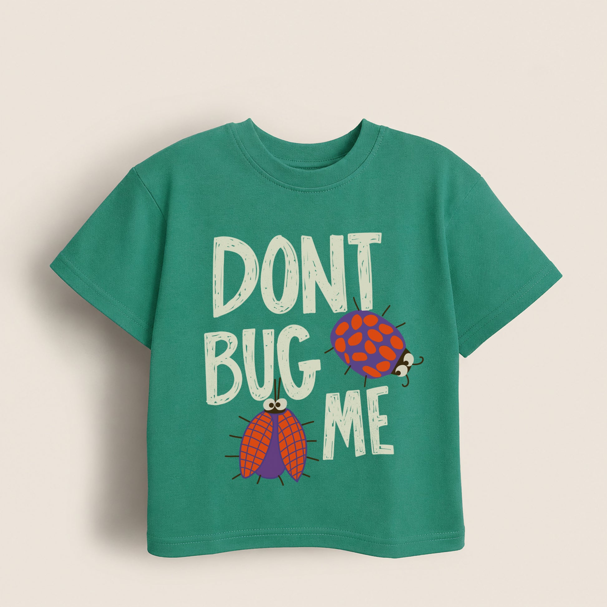 Green kids t-shirt with 'Don't Bug Me' text and ladybug graphics on a beige background