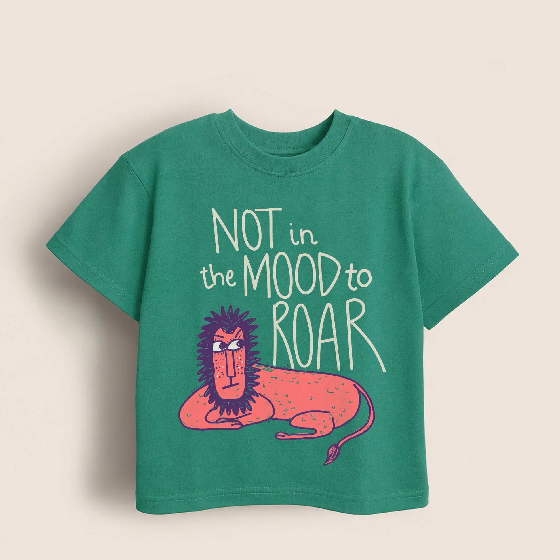 Green kids t-shirt with a lion graphic and 'Not in the mood to roar' text on it on a beige background
