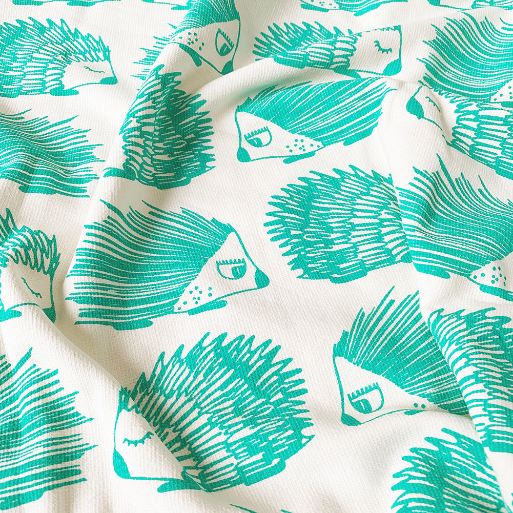 
A close up of a Mapayah cotton bath towel featuring a green porcupine print, neatly folded to show the design, fabric quality, and softness.
