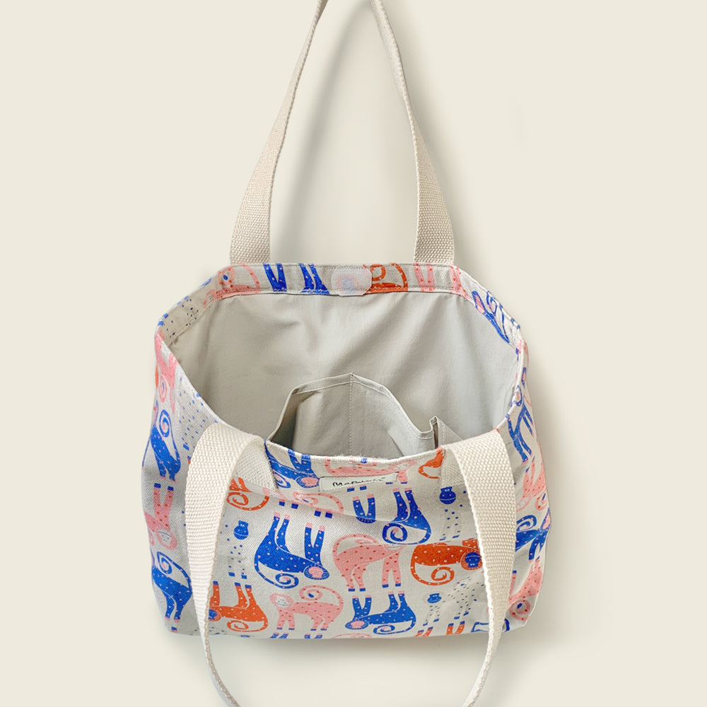 A canvas tote bag with a cream-colored interior and handles, featuring a whimsical pattern of blue and orange monkey on a white background.