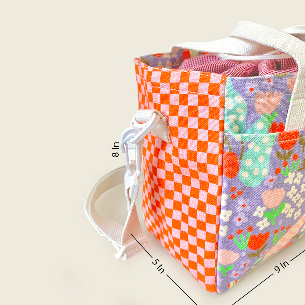 A fabric lunch bag with multiple colorful patterned panels, including orange and white checkers and a floral print on lavender, shown with white straps and overlaid dimension lines indicating 8 in height, 5 in width, and 9 in depth.