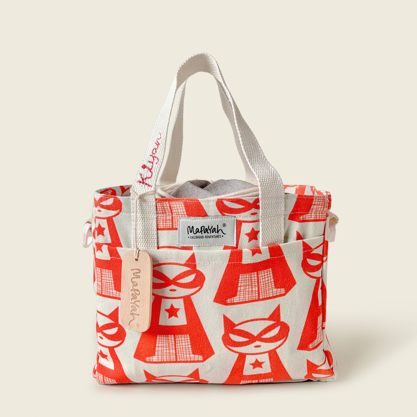 A canvas lunch bag featuring a red super cat pattern, with off-white fabric handles and a visible 'Mapayah' brand label and personalised name on bag strap.