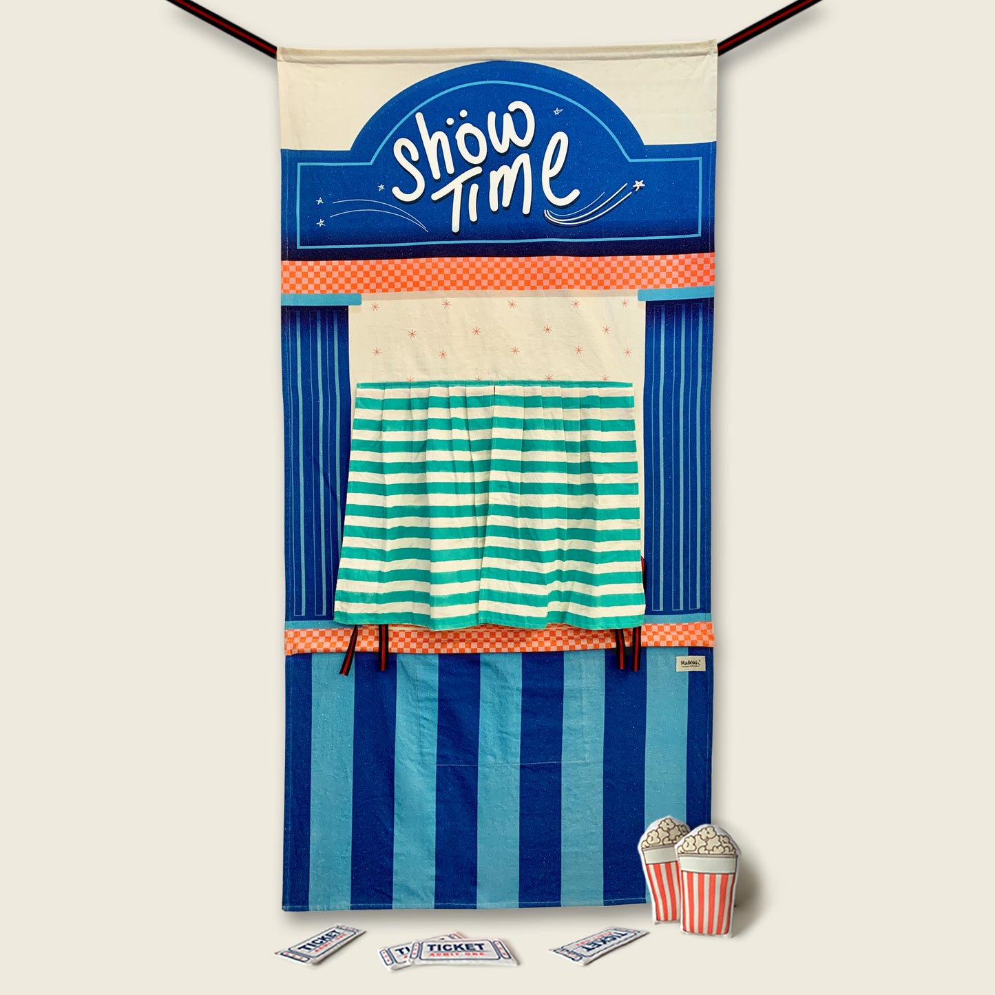 A blue-striped puppet theatre doorway curtain with an arched "Show Time" marquee, an orange checkered trim, and green and white striped stage curtains tied open, with stuffed popcorn and ticket props resting at the base against a solid cream background.