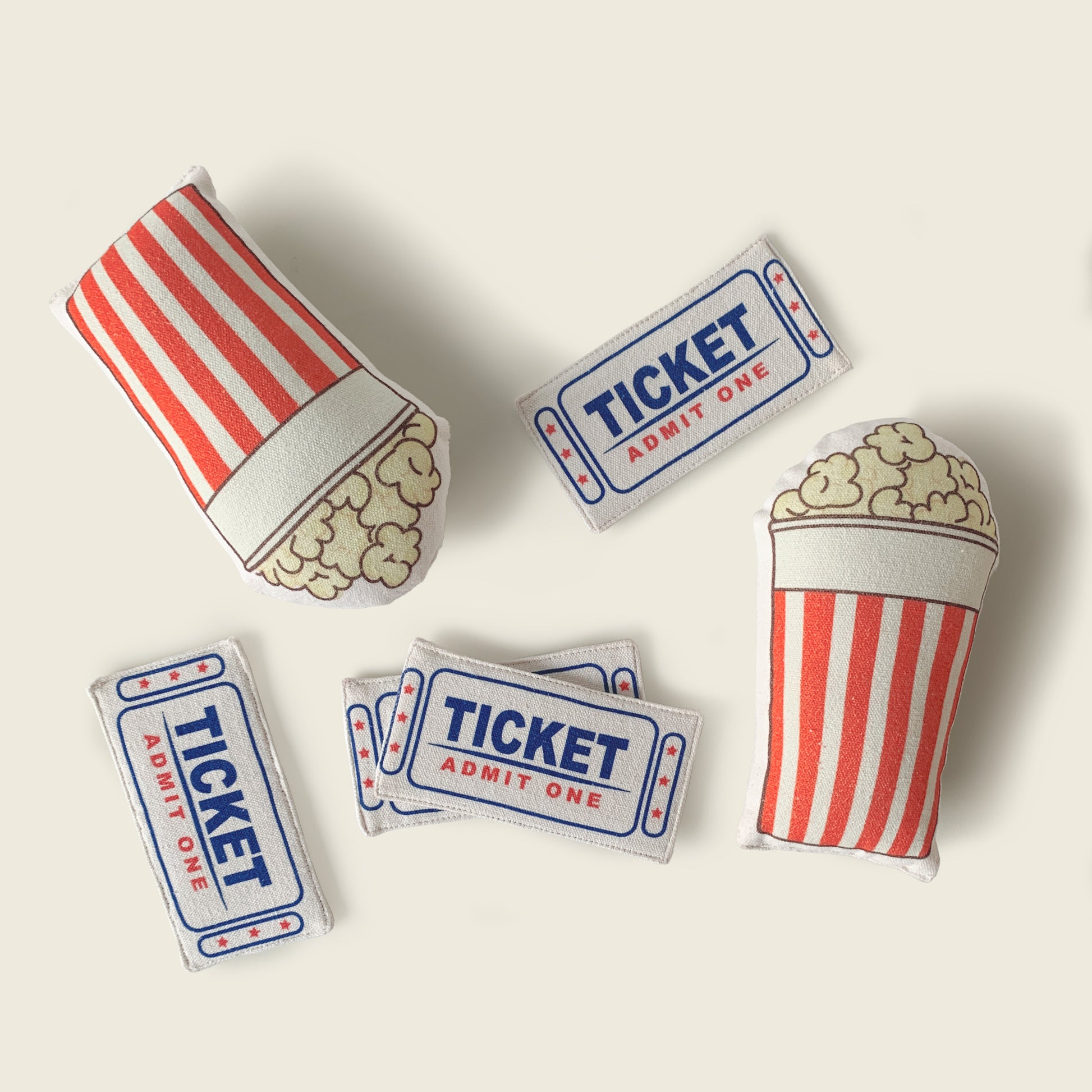 stuffed play props included with the Mapayah STAGE Theatre: two striped popcorn buckets and four "Ticket Admit One" tickets, laid out on a solid cream background.