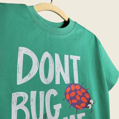 Close-up of green t-shirt with 'Don't Bug Me' text and ladybug graphic on a beige background