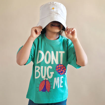 Child wearing a green t-shirt with 'Don't Bug Me' text and a white bucket hat with a flower design.